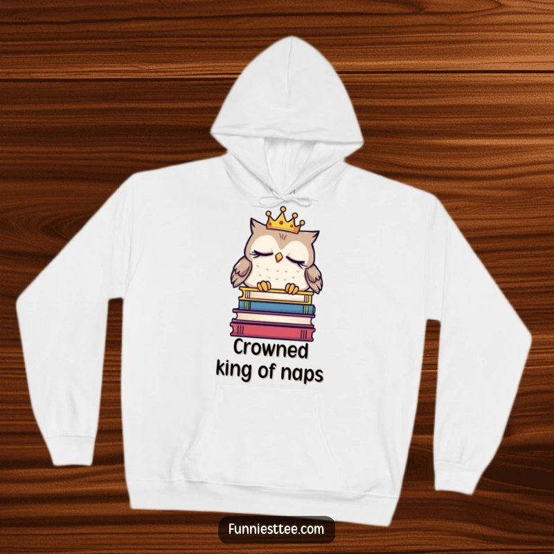 Funny sleepy owl hoodie wearing a crown, dozing on a book stack, providing warm, humorous comfort for lovers of literature and naps.