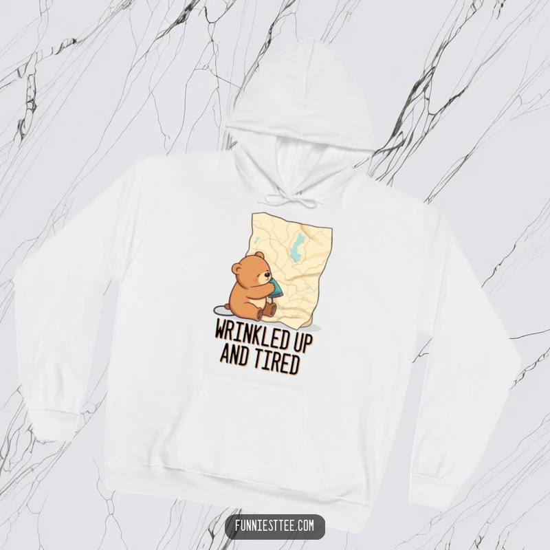 Funny hoodie showing a very sleepy bear attempting to iron out the considerable wrinkles on a vast map, highlighting a moment of gentle chaos.